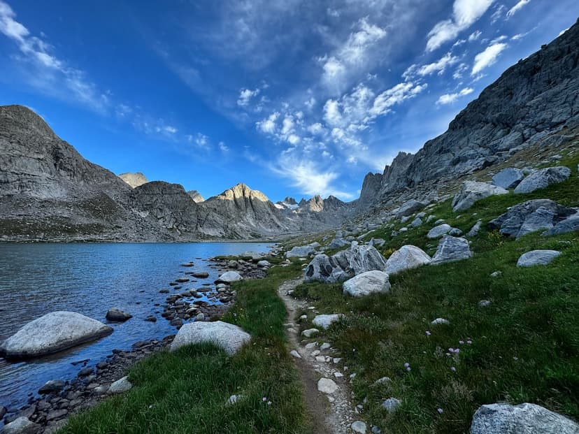 Photo of Katy nearing the top of a mountain pass in the Wind River Range near sunrise, many mountains and lakes behind her